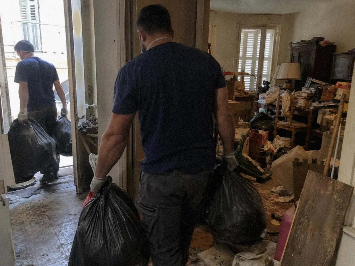 Deux ouvriers évacuant des sacs d'un logement très encombré